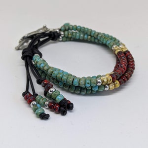 May include: A multi-strand bracelet with turquoise, red, and yellow beads. The bracelet has a leather closure with a silver accent.