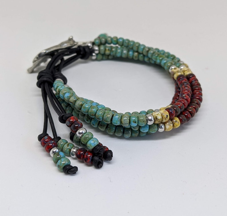 May include: A multi-strand bracelet with turquoise, red, and yellow beads. The bracelet has a leather closure with a silver accent.