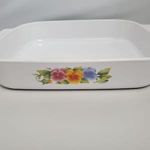 May include: White rectangular baking dish with a floral design featuring pink, yellow, and blue pansies. The dish has two handles and is suitable for baking and serving. A classic kitchenware item.