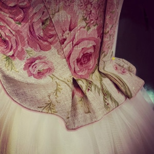 May include: A white tulle skirt with a pink floral fabric bodice. The bodice has a gathered design and a pink trim.