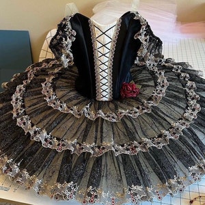 May include: A black and gold ballet tutu with a black velvet bodice and a red rose accent. The tutu is made of layers of tulle and has a delicate lace trim.