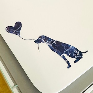 May include: A white printer with a blue and white marble design sticker of a dog holding a heart-shaped balloon. The text "Blue Water" is written in blue ink on the printer.