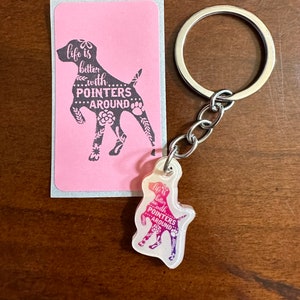 May include: A pink and white card with a black silhouette of a dog with the text "Life is better with pointers around". A clear keychain with a colorful dog silhouette with the same text is attached to a silver key ring.