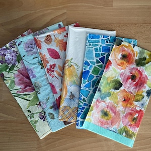 May include: Six different patterned paper napkins with a blue border. The patterns include floral, geometric, and autumnal themes.