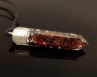 Puede incluir: Un collar con colgante de cristal rectangular transparente y tapa plateada, suspendido de un cordón negro. El cristal está lleno de inclusiones rojo oscuro, creando un contraste. El colgante mide aproximadamente 4 cm de largo.