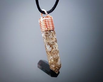 Puede incluir: Un colgante de cristal dorado y blanco con un envoltorio de alambre de cobre, colgando de un cordón negro.