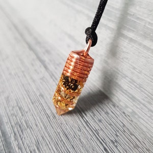 May include: A copper wire wrapped crystal pendant with gold flakes inside, hanging from a black cord.