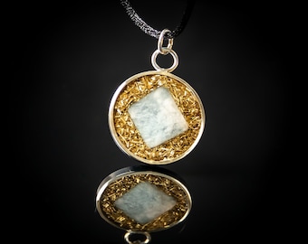 May include: A silver pendant with a square-shaped blue gemstone set in a gold-toned frame. The pendant is on a black cord.