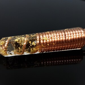 May include: A clear quartz crystal pendant with gold flakes and copper wire wrapped around it. The pendant is attached to a black cord.