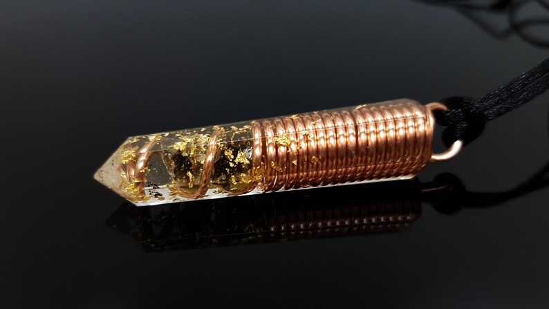 May include: A clear quartz crystal pendant with gold flakes and copper wire wrapped around it. The pendant is attached to a black cord.