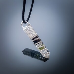 May include: A silver wire-wrapped pendant with clear quartz, black tourmaline, and green aventurine crystals. The pendant is attached to a black cord.