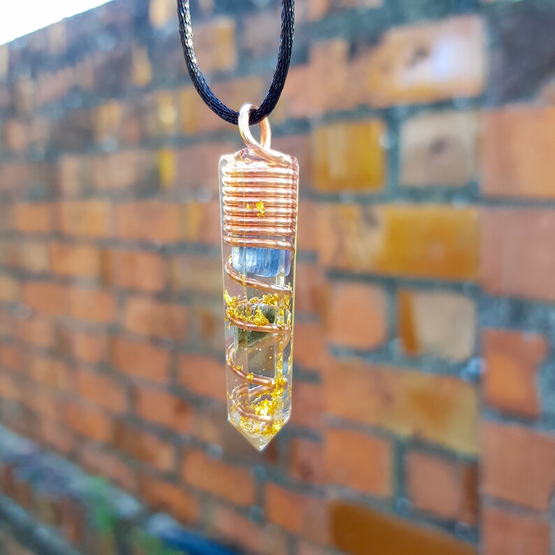 May include: A clear crystal pendant with copper wire wrapped around it. The crystal is filled with gold flakes and a blue stone. The pendant is hanging from a black cord.