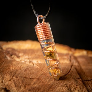 May include: A clear crystal pendant with a copper wire wrapped around it. The pendant is filled with gold flakes and blue and green crystals. The pendant is hanging from a black cord.