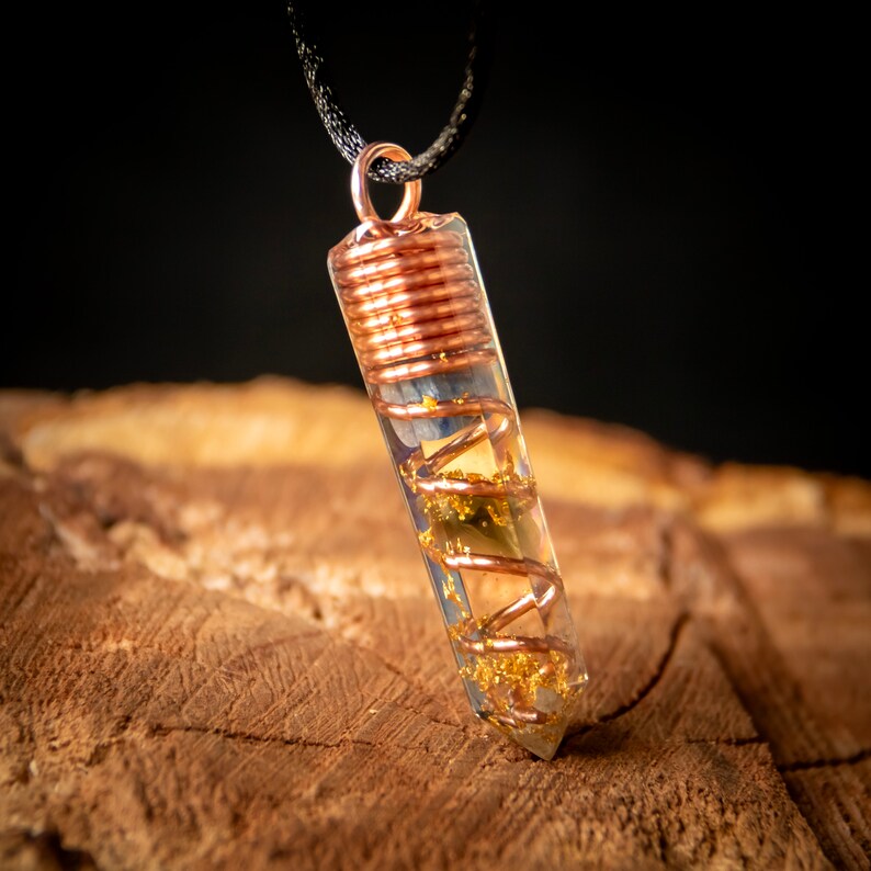 May include: A clear crystal pendant with a copper wire wrapped around it. The pendant is filled with gold flakes and blue and green crystals. The pendant is hanging from a black cord.