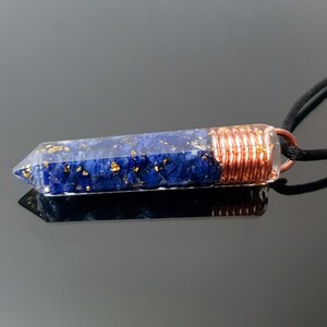 May include: A blue and gold crystal pendant with copper wire wrapping, hanging from a black cord.