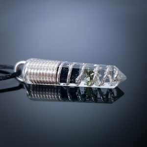 May include: A silver wire wrapped crystal pendant with black and green inclusions. The pendant is attached to a black cord.