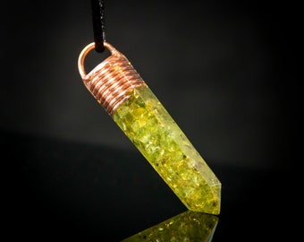 Op de afbeelding: Een hanger met koperdraad gewikkeld met een groene peridot-kristalpunt. De hanger hangt aan een zwart koord.