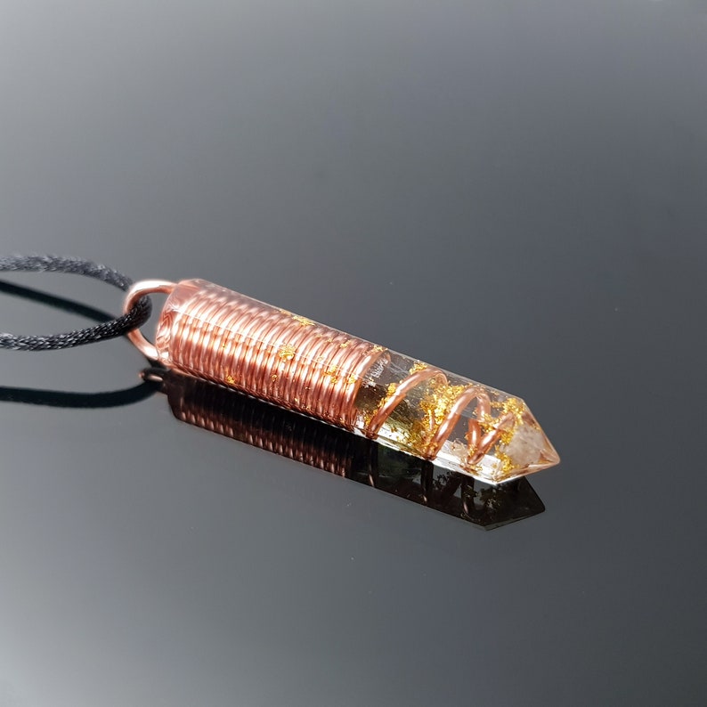 May include: A clear quartz crystal pendant with gold flakes embedded in the resin. The crystal is wrapped in copper wire and attached to a black cord.