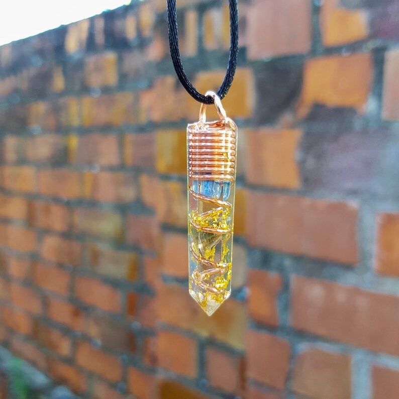 May include: A gold and copper wire wrapped pendant with a clear crystal filled with gold flakes. The pendant is hanging from a black cord.