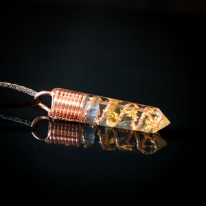 May include: A clear quartz crystal point wrapped in copper wire with gold leaf accents. The crystal is suspended from a black cord.