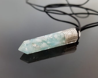 May include: A light blue crystal pendant with silver wire wrapping, hanging from a black cord.