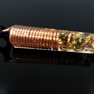 May include: A clear quartz crystal pendant with a copper wire coil encased in resin and gold flakes. The pendant is attached to a black cord.
