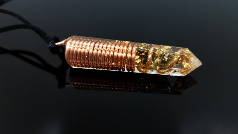 May include: A clear quartz crystal pendant with a copper wire coil encased in resin and gold flakes. The pendant is attached to a black cord.