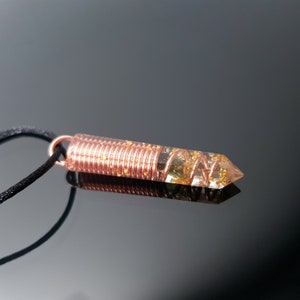 May include: A copper wire wrapped around a clear quartz crystal pendant with gold flecks. The pendant is attached to a black cord.