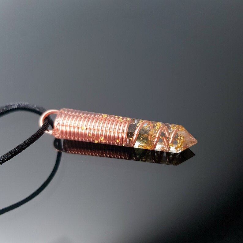May include: A copper wire wrapped around a clear quartz crystal pendant with gold flecks. The pendant is attached to a black cord.
