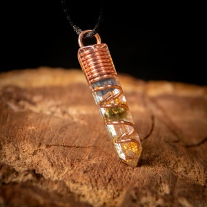 May include: A clear quartz crystal pendant with gold flakes and copper wire wrapped around it. The pendant is hanging from a black cord.