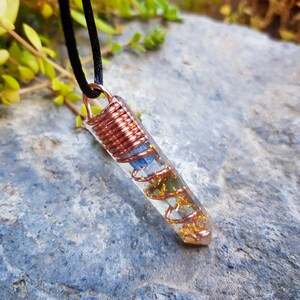 May include: A clear quartz crystal pendant with copper wire wrapped around it. The crystal contains gold flakes and a blue stone inside. The pendant is hanging from a black cord.