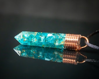 May include: A teal blue pendant with copper wire wrapping, filled with small teal blue and gold flecks. The pendant is attached to a black cord.