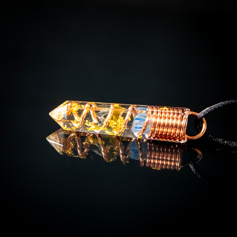 May include: A clear quartz crystal pendant with gold flakes and copper wire wrapped around it. The pendant is attached to a black cord.