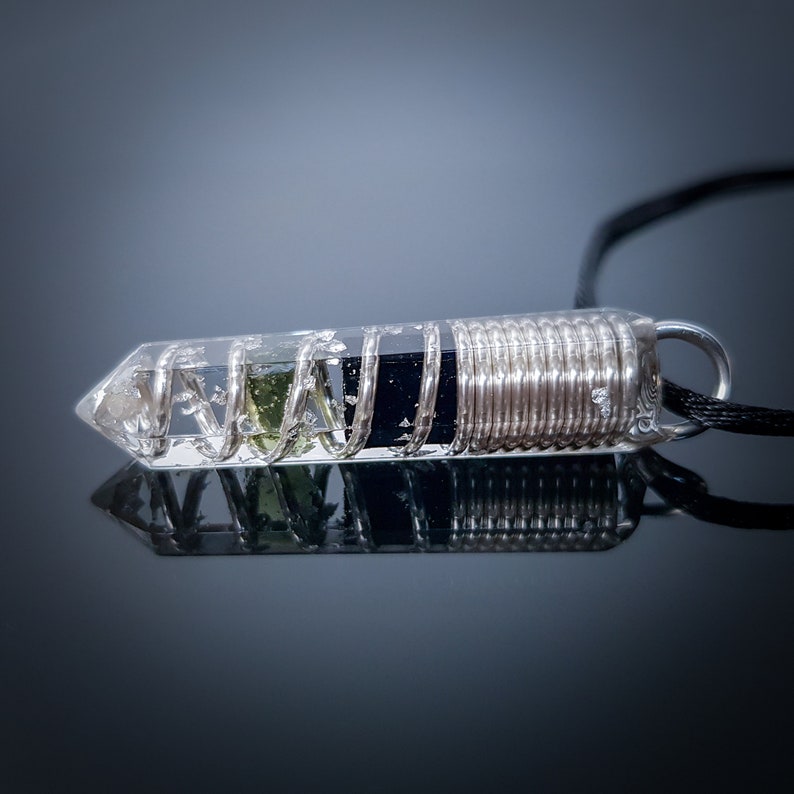 May include: A clear crystal pendant with a silver wire coil wrapped around a black stone and a green stone inside. The pendant is on a black cord.