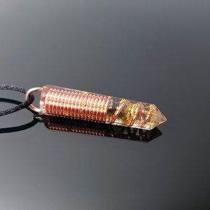 May include: A clear quartz crystal pendant with gold flakes and copper wire wrapped around it. The pendant is attached to a black cord.