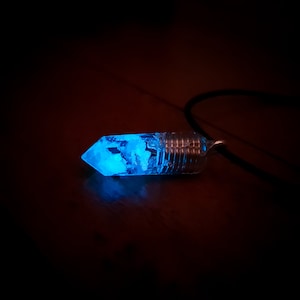 Könnte beinhalten: Eine leuchtende blaue Kristall-Halskette mit einer silbernen Drahtumwicklung. Der Kristall ist klar und hat eine strukturierte Oberfläche.