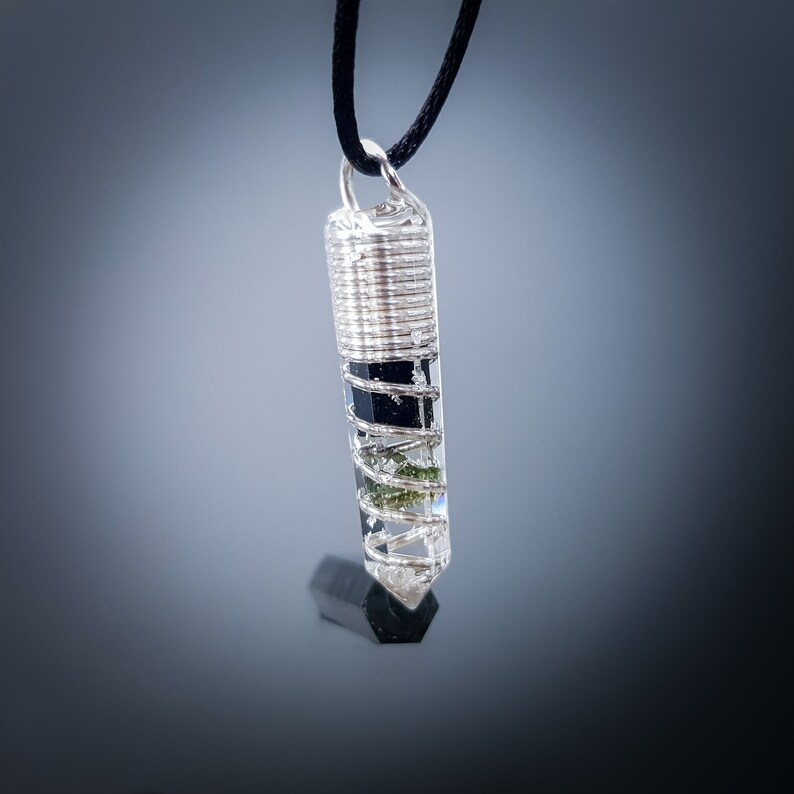 May include: A silver wire-wrapped crystal pendant with black and green inclusions. The pendant is hanging from a black cord.