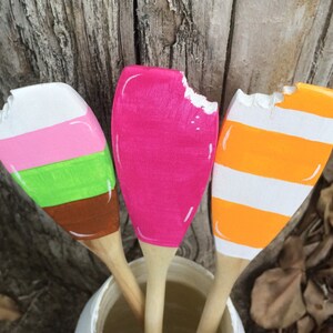 Puede incluir: Tres cucharas de madera pintadas para parecer helado. Las cucharas est&aacute;n pintadas de rosa, naranja y verde con rayas blancas. Las cucharas est&aacute;n dispuestas en un jarr&oacute;n.
