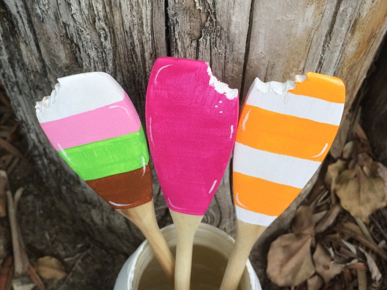 Puede incluir: Tres cucharas de madera pintadas para parecer helado. Las cucharas est&aacute;n pintadas de rosa, naranja y verde con rayas blancas. Las cucharas est&aacute;n dispuestas en un jarr&oacute;n.