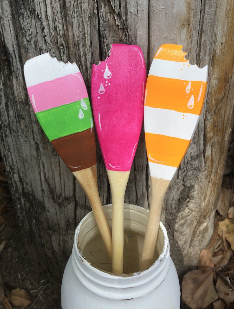Puede incluir: Tres cucharas de madera pintadas para parecer conos de helado. Las cucharas est&aacute;n en un tarro blanco y tienen un mordisco en la parte superior. Los sabores de helado son rosa, naranja y verde.