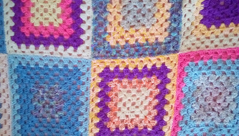 May include: A colorful crocheted blanket made of squares in various shades of blue, pink, purple, and yellow.