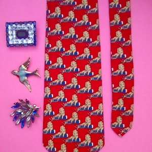 May include: A red silk tie with a repeating pattern of gold lions. The tie has a blue and white trim. The tie is on a pink background.