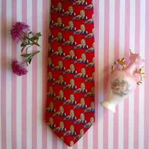 May include: A red silk tie with a repeating pattern of gold lions. The tie is on a pink and white striped background.