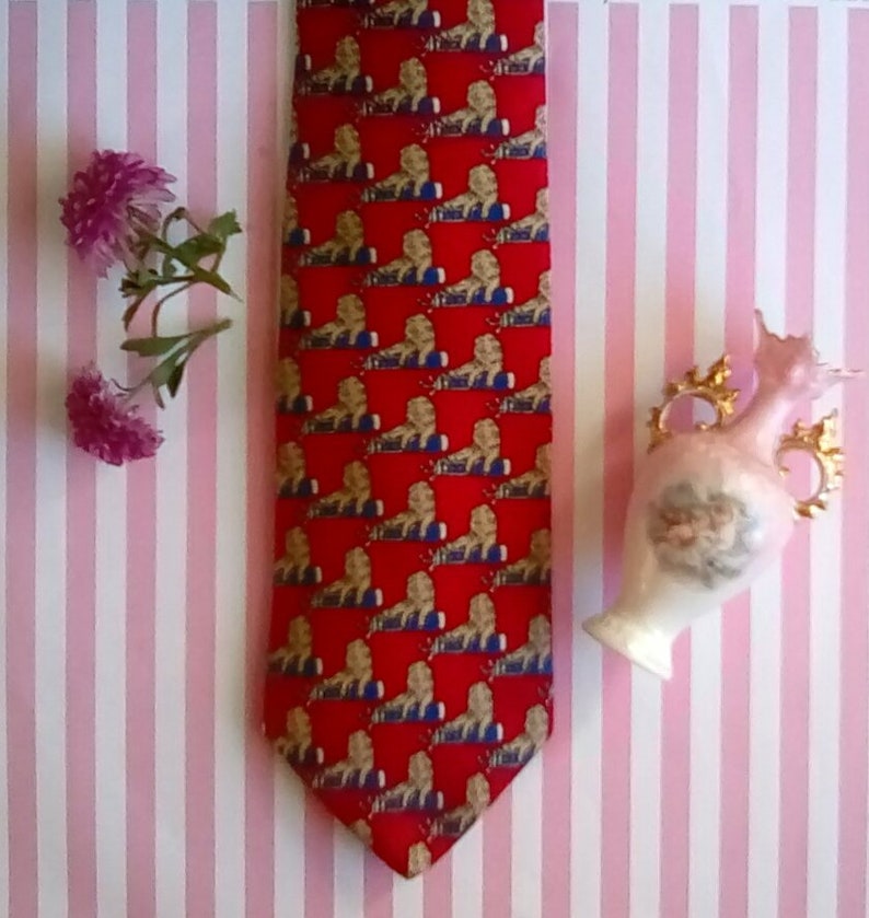 May include: A red silk tie with a repeating pattern of gold lions. The tie is on a pink and white striped background.