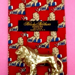 May include: Red silk tie with a repeating pattern of lions holding golf clubs. The tie has a black label that reads "Brooks Brothers Makers All Silk Made in U.S.A."
