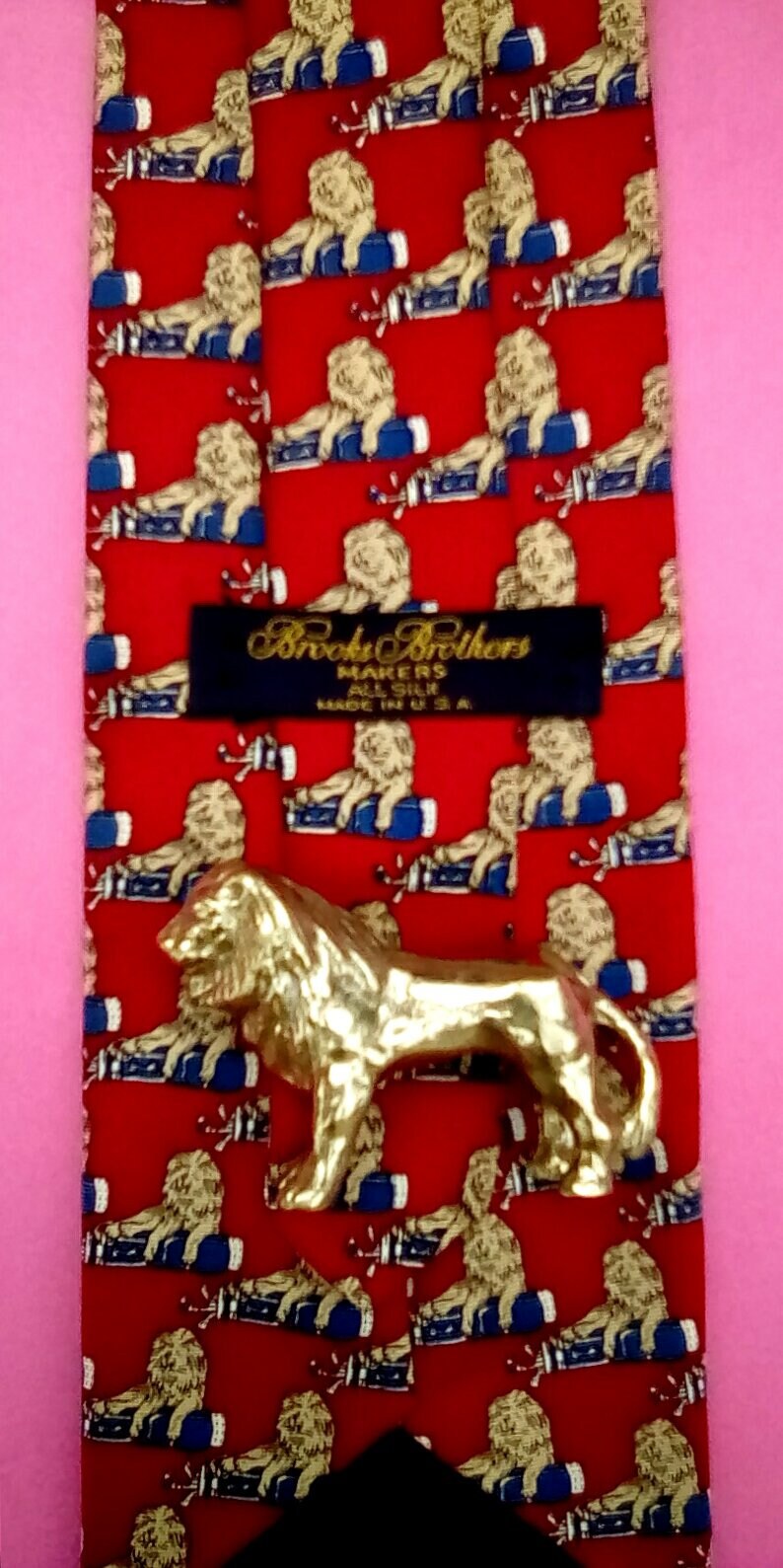 May include: Red silk tie with a repeating pattern of lions holding golf clubs. The tie has a black label that reads "Brooks Brothers Makers All Silk Made in U.S.A."