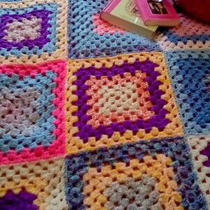 May include: A colorful crocheted blanket with squares in shades of blue, pink, yellow, purple, and white. The blanket is made with a granny square pattern.