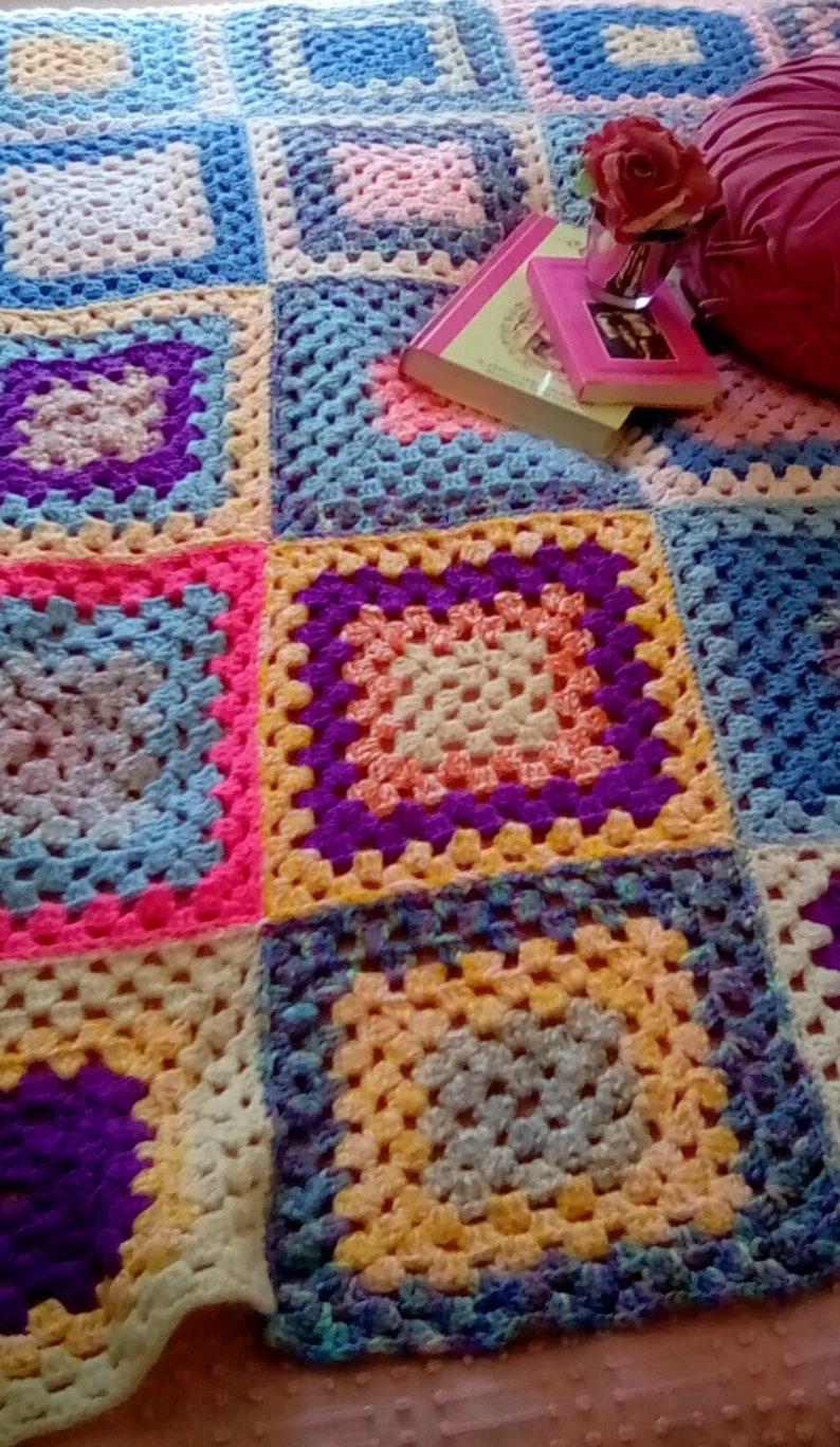 May include: A colorful crocheted blanket with squares in shades of blue, pink, yellow, purple, and white. The blanket is made with a granny square pattern.