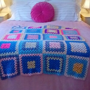 May include: A pink bed with a white and pink striped bedspread and a pink crocheted throw blanket with colorful squares. A pink round pillow is on top of the bedspread.