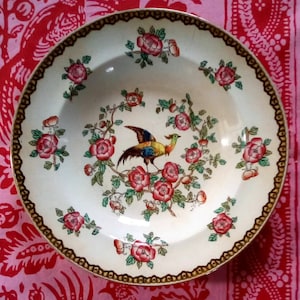 May include: A white ceramic soup bowl with a gold rim and a colorful floral design featuring a pheasant. The bowl has a white background with a gold rim and a colorful floral design featuring a pheasant.